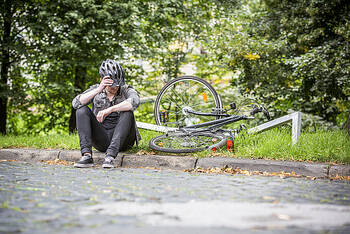 Radfahrer sitzt am Wegrand nach einem Sturz mit kaputtem Fahrrad